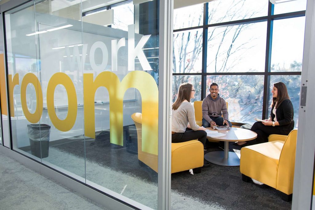 Image of three individuals around a low table in a glassed study room.