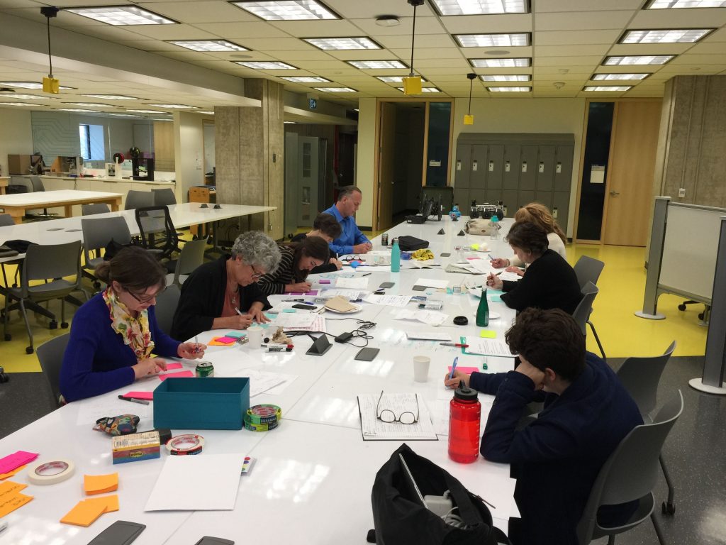 Image of a group of people around a table, writing on sticky notes.